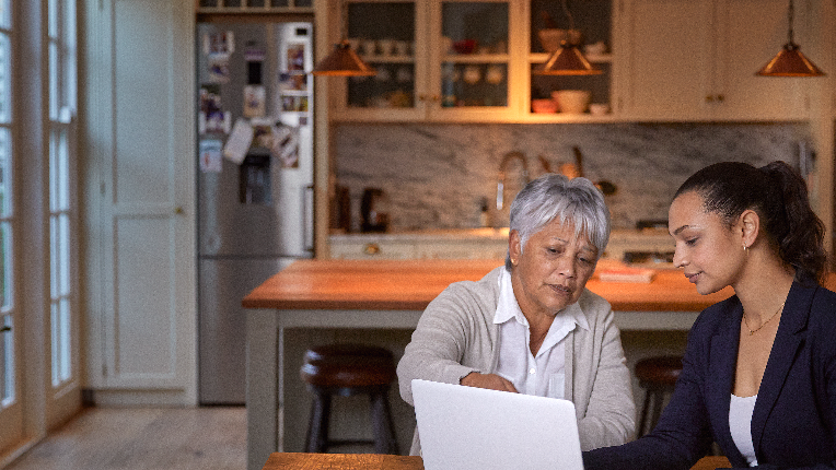 Mother and adult daughter looking at a laptop in kitchen.