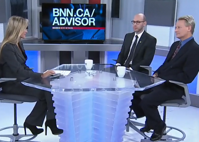 Three business professionals on a TV set sitting at a clear round table with a TV behind them